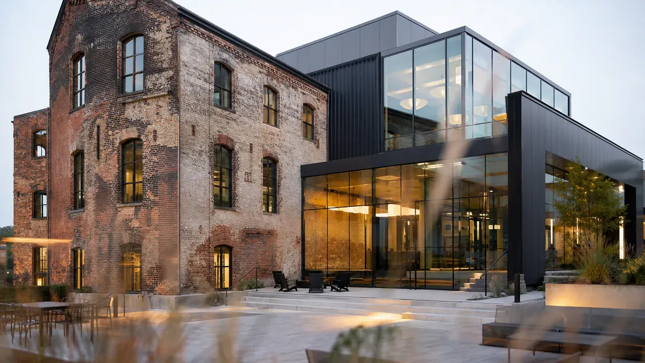 Altes Ziegelgebäude mit modernem Anbau, verwitterte Fassade trifft auf eine Glasfläche